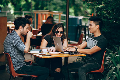 millennials sitting around a table drinking coffee and using a laptop