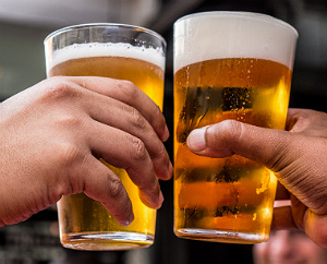 Two beer drinkers clink their glasses of beer together a the bar