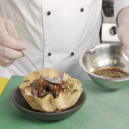 Chef Chris John spoons hoisin and sesame seed dressing from a chrome bowl onto a salad in an edible bowl