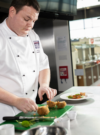 Chef Chris John wears blue gloves and coats the eggs in flour