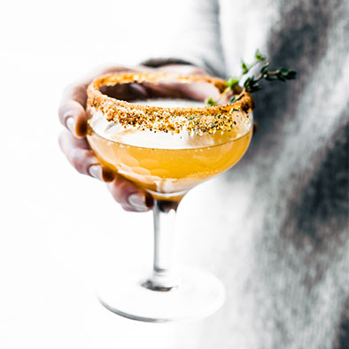 person holding an orange mocktail finished with a herb sprig and a dusted rim