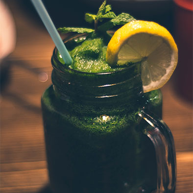 green juice smoothie in a mason jar with lemon and mint garnish