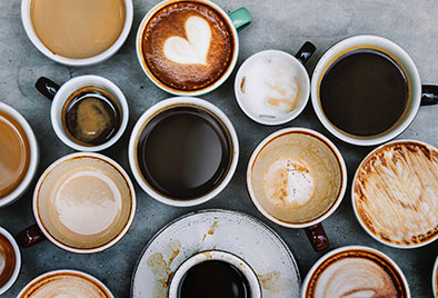 several cups of coffee in different mugs on a slate background