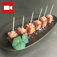 A cube of paneer cheese fried in honey and molasses and dipped in coconut