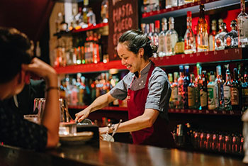 Hospitality worker smiling when preparing drinks behind bar