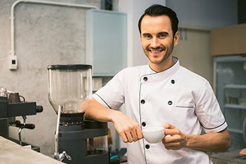 Hospitality worker smiling posing next to blender with cup of coffee in hand