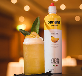 A Bottle Of Banana-Flavoured ODK Cocktail Puree Next To A Freshly Prepared Cocktail